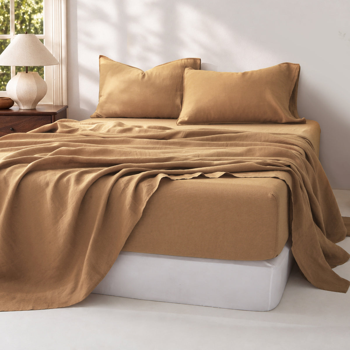Sandy Beige 100% linen sheet set displayed on a bed, with natural fabric wrinkles illuminated by soft sunlight.